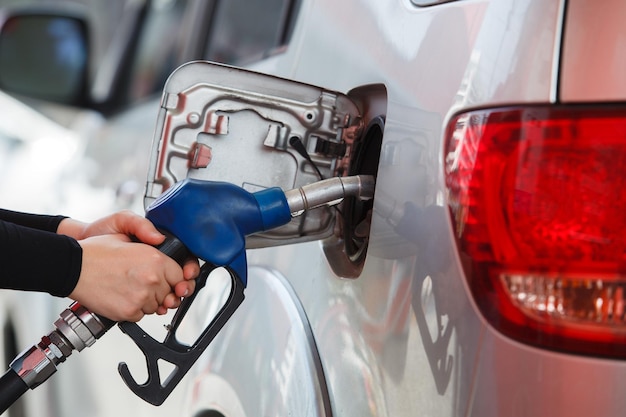 Mulher em close-up manuseia de bombeamento de bico de combustível de gasolina no tanque para carro em estação de gasolina