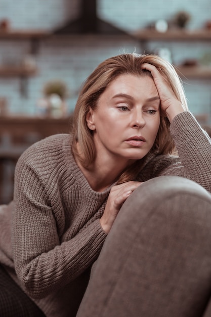 Mulher em desespero. Mulher madura atraente de olhos escuros sentada no sofá e desesperada