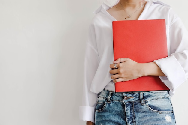 Mulher em estilo casual segura livro com capa vermelha vazia nas mãos simulada para educação e estilo de vida