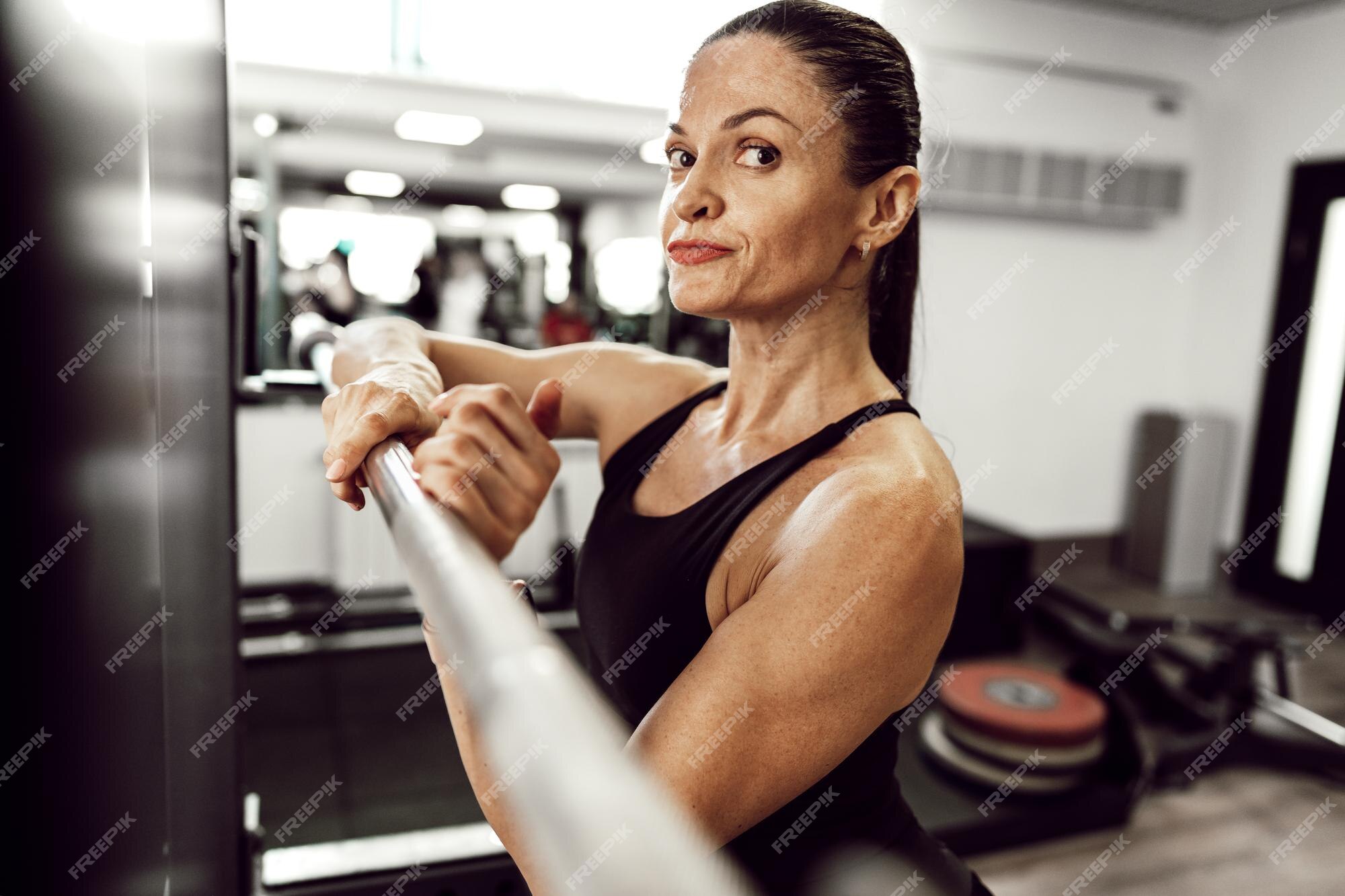 Uma foto de corpo inteiro da mulher esportiva que está subindo a barra para  fazer agachamentos na prateleira de agachamento em uma academia. uma menina  morena musculosa usando um top coral e