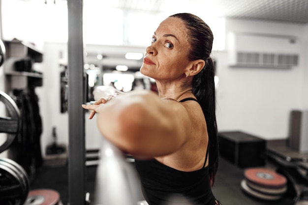 Foto mulher em forma fazendo agachamentos com barra em uma academia