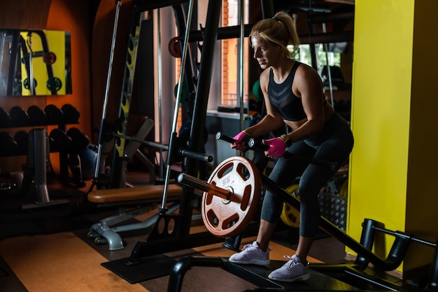 Mulher em forma se exercitando na academia usando o treino de remo nas costas com barra em T