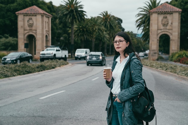 mulher em frente à entrada de uma universidade segurando uma xícara de café.