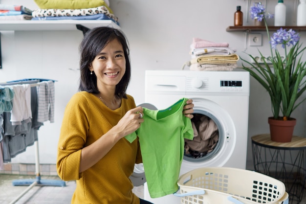 Mulher em frente à máquina de lavar, sorrindo para a câmera enquanto lava a roupa carregando roupas dentro