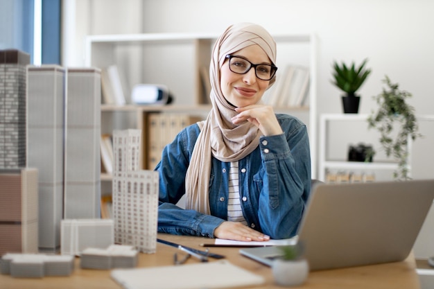 Mulher em hijab sentada na mesa de escritório com aparelhos modernos