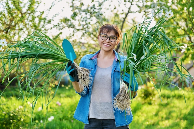 Mulher em luvas de jardinagem com planta de narciso branco e pá fêmea olhando para a câmera