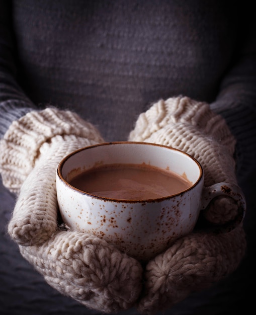 Mulher em luvas segurando uma xícara de chocolate quente. Foco seletivo