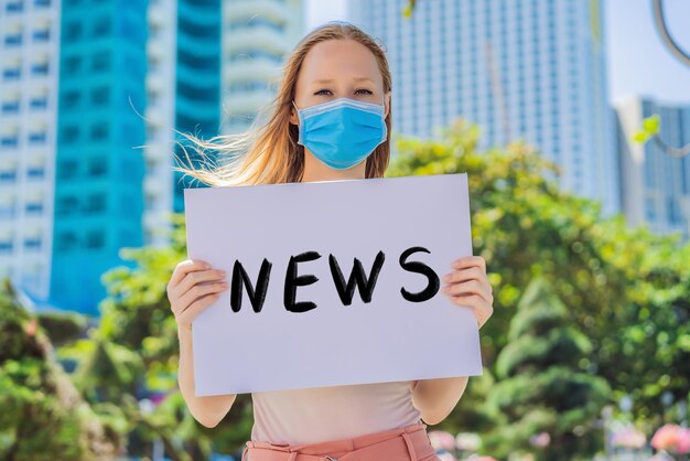 Foto mulher em máscara médica previne doença de coronavírus segura um cartaz de notícias de texto escrito à mão isolado em branco conceito de coronavírus covid-19