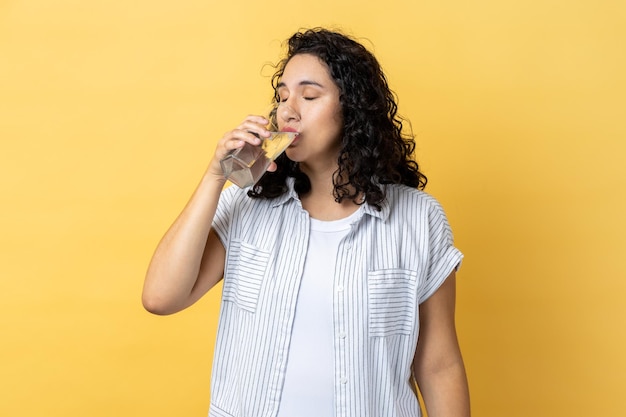 Mulher em pé bebendo água de vidro desfrutando de bebidas frescas mantém os olhos fechados