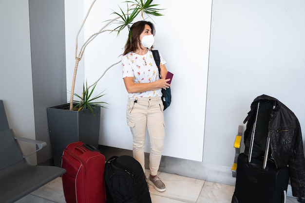 Mulher em pé com máscara protetora esperando no saguão do aeroporto Mulher casual tem passaporte