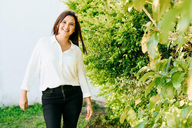 Mulher em pé e posando com uma parede branca e plantas