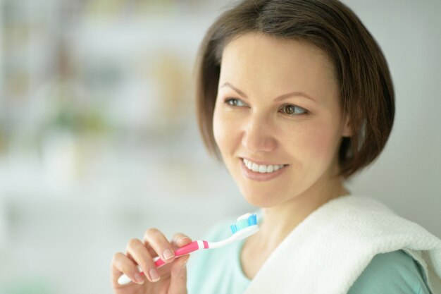 Mulher em pé no banheiro e escovando os dentes.