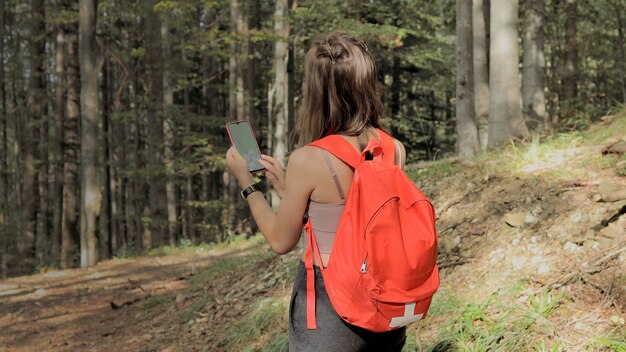 Mulher em pé no meio da floresta, usando aplicativo de navegação no smartphone