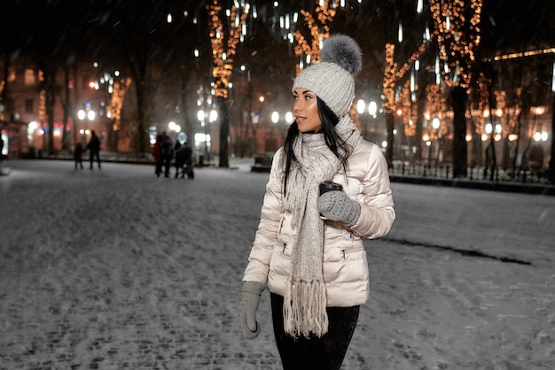 mulher em roupas de inverno elegante com uma xícara de café ao ar livre.