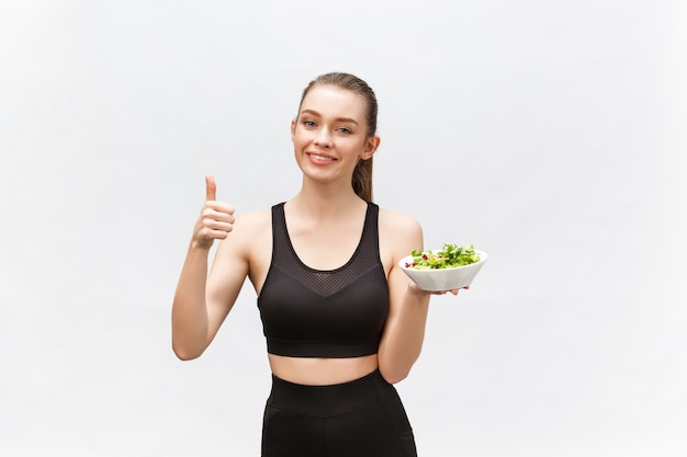 Mulher em roupas esportivas com salada, aparecendo o polegar, isolada