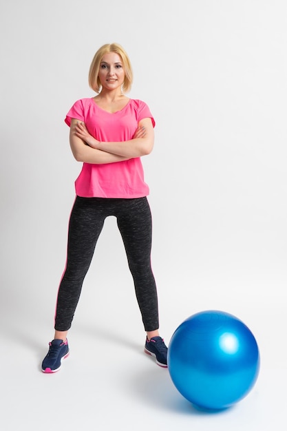 Mulher em roupas esportivas e tênis pratica esportes com uma bola de fitness