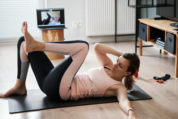 Mulher em roupas esportivas faz exercícios cardiovasculares em casa usando laptop