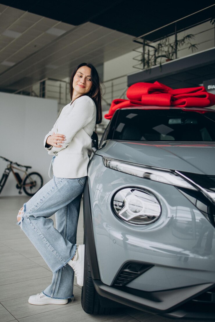 Foto mulher em showroom de carros de pé ao lado de seu carro novo com laço vermelho