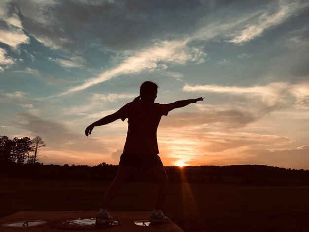 Foto mulher em silhueta com os braços estendidos de pé contra o céu durante o pôr do sol