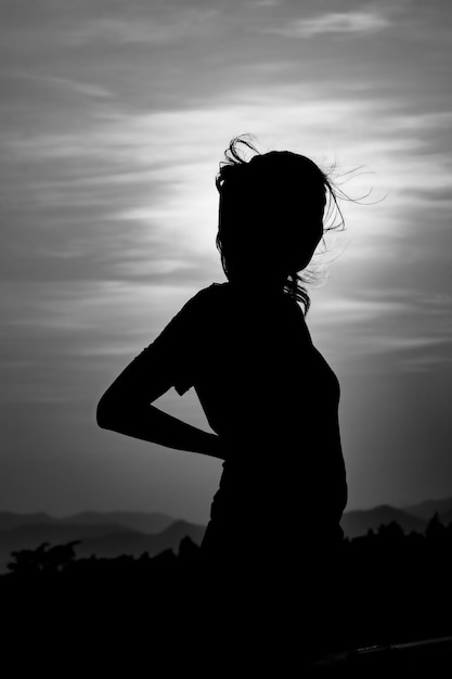 Foto mulher em silhueta de pé contra o céu ao pôr-do-sol