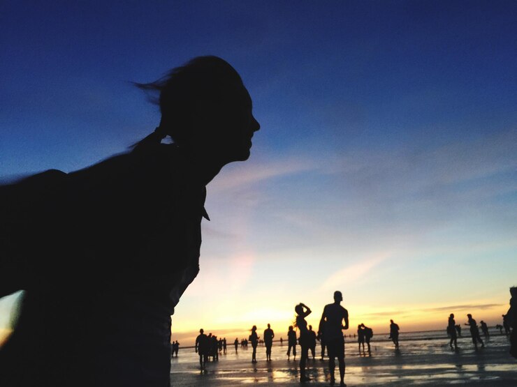 Foto mulher em silhueta de pé na praia contra o céu durante o pôr do sol
