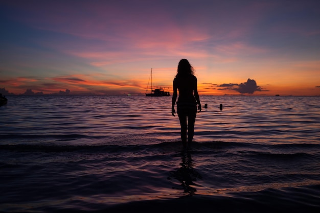 Mulher em silhueta de pé na praia durante o pôr do sol