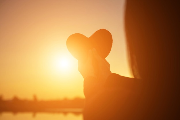 Foto mulher em silhueta em forma de coração contra o céu durante o pôr do sol
