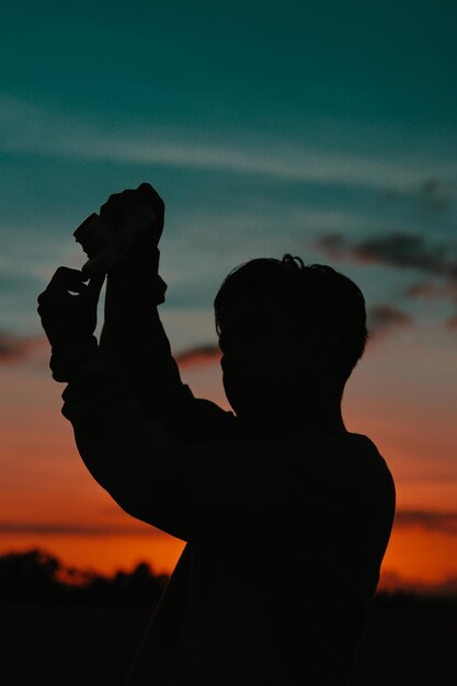 Foto mulher em silhueta fotografando contra o céu durante o pôr do sol