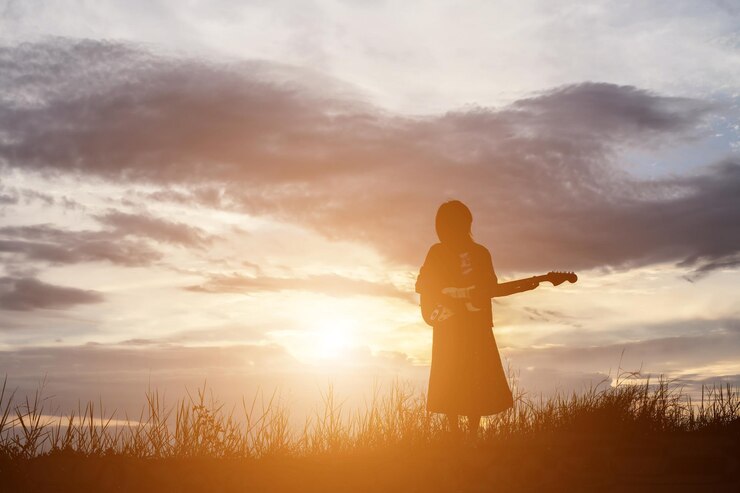 Foto mulher em silhueta tocando guitarra enquanto está de pé em terra contra o céu durante o pôr do sol