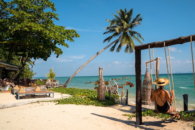 Foto mulher em sua fuga romântica da lua de mel isolada em uma praia paradisíaca com palmeiras. resort de luxo caro para casais e pessoas solteiras. relaxe em um balanço. viajar para o conceito de tailândia.