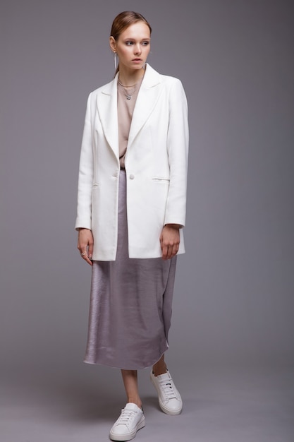 Mulher em tênis de jaqueta branca longa prata metálica com saia de tênis Fundo cinza Fotografia de Estúdio Retrato