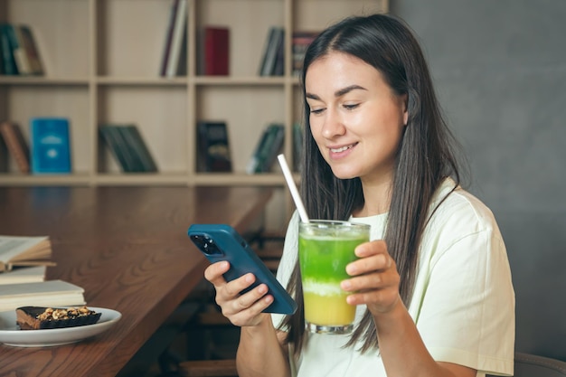 Mulher em um café com um smartphone e um copo de limonada