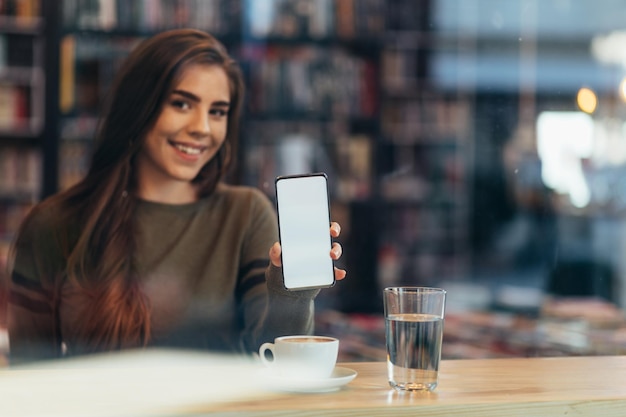 Mulher em um café segurando e mostrando a tela branca do smartphone