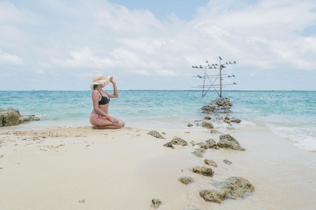 Foto mulher em um maiô sentado na praia ensolarada com o mar do caribe colombiano ao fundo