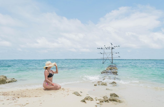 Foto mulher em um maiô sentado na praia ensolarada com o mar do caribe colombiano ao fundo