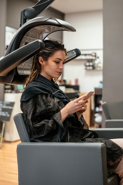 Mulher em um secador de cabelo infravermelho de cabeleireiro profissional