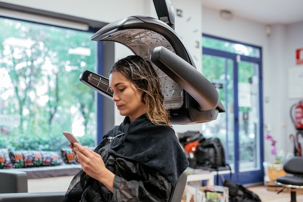 Mulher em um secador de cabelo infravermelho de cabeleireiro profissional