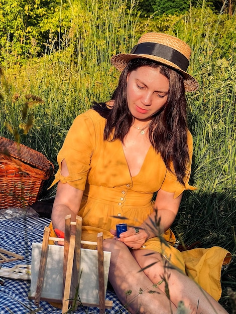 mulher em um vestido amarelo ensolarado e chapéu pinta no piquenique