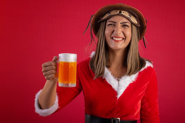 Foto mulher em um vestido de papai noel, um chapéu nordeste brasileiro e um copo de cerveja em um fundo vermelho