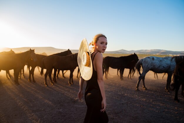 Mulher em um vestido preto entre cavalos selvagens