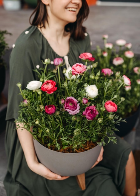 Mulher em uma floricultura segurando um grande vaso de flores com flores de ranúnculo rosa fechadas