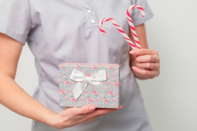 Mulher em uniforme médico com caixa de presente e doces de Natal