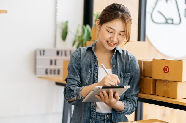 Mulher embalando um item que ela vende on-line Jovem proprietário de uma pequena empresa embalando uma caixa de papelão no local de trabalho Mulher vendedora freelance prepara uma caixa de pacotes de produto para entrega ao cliente