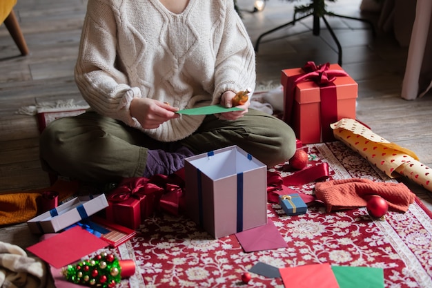 Mulher embrulhando presentes de Natal em casa no chão.