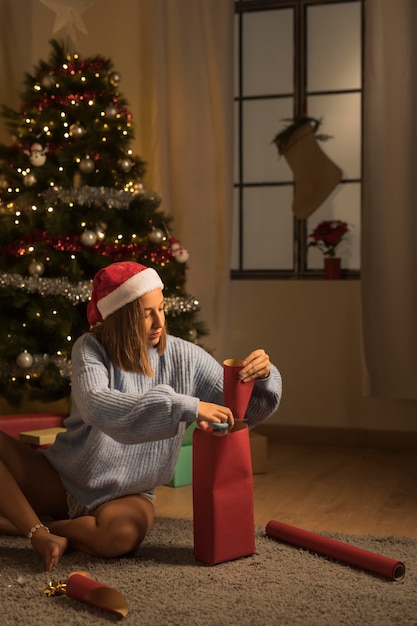 Mulher embrulhando presentes para o Natal com chapéu de Papai Noel