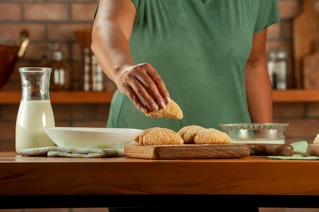 Mulher empanando carne brasileira recheada de croquete risolis de carne em uma mesa de madeira Vista superior