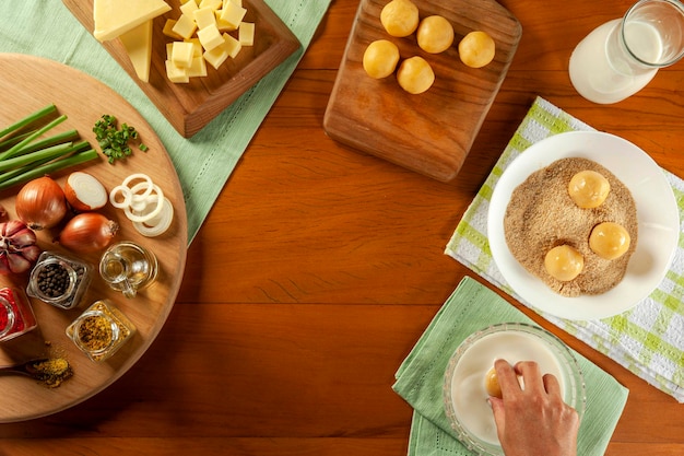 Mulher empanando queijo brasileiro recheado croquete bolinha de queijo em uma mesa de madeira vista superior