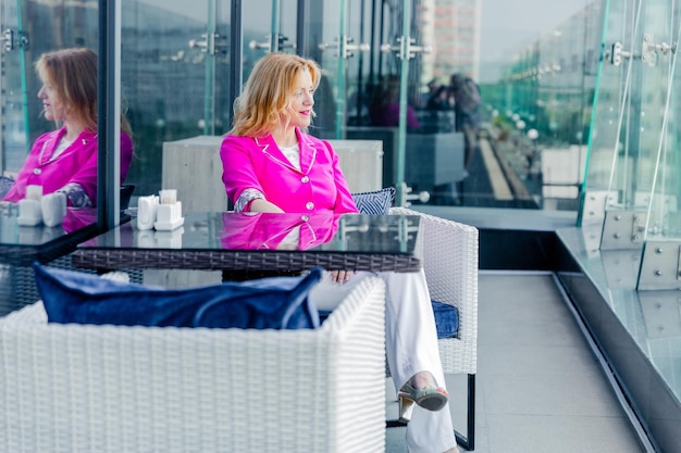 Mulher empreendedora de sucesso em uma jaqueta magenta posando no terraço de um café em um centro de negócios