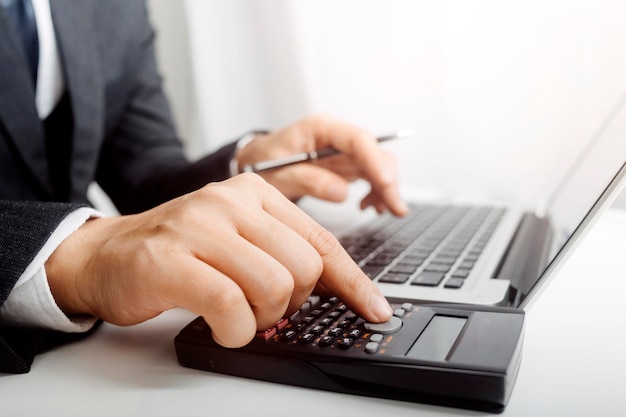 Mulher empreendedora usando uma calculadora com uma caneta na mão calculando despesas financeiras em home office