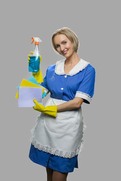 Mulher empregada atraente segurando spray de limpeza. Retrato de corpo inteiro de mulher de limpeza sorridente, mostrando trapos e o frasco de detergente.